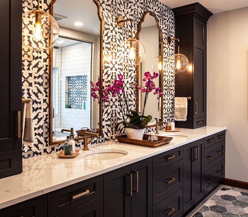 Black and white encaustic tiles, gold-rimmed arch mirrors, and dark cabinetry give old world charm to this sumptuous bathroom.