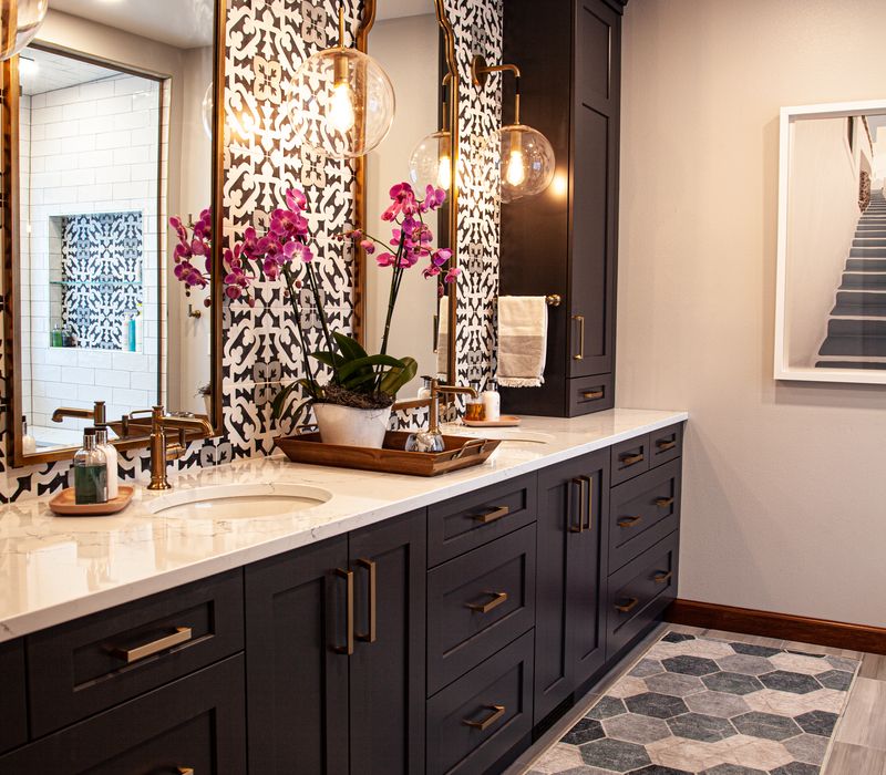 Black and white encaustic tiles, gold-rimmed arch mirrors, and dark cabinetry give old world charm to this sumptuous bathroom.