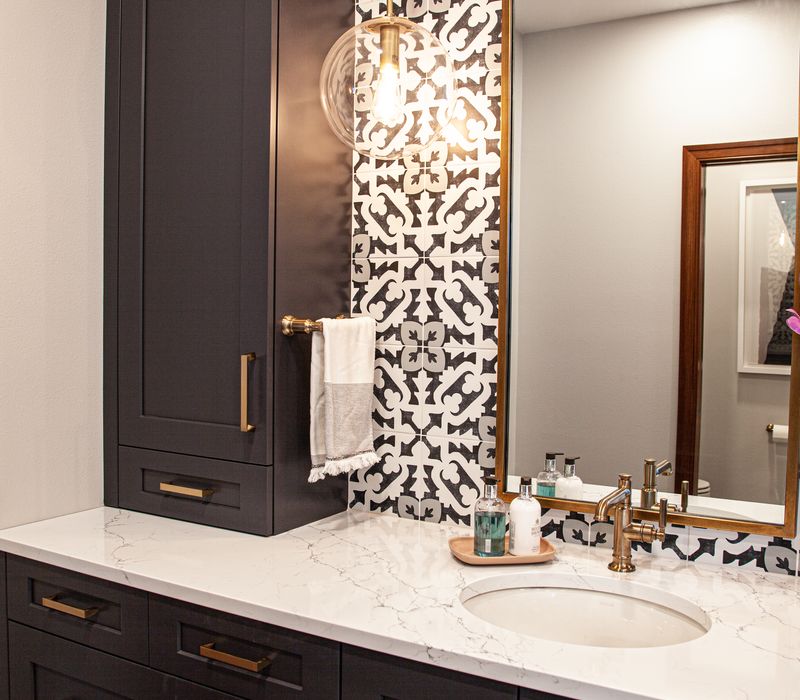 Black and white encaustic tiles, gold-rimmed arch mirrors, and dark cabinetry give old world charm to this sumptuous bathroom.