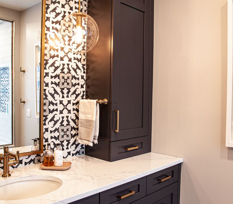 Black and white encaustic tiles, gold-rimmed arch mirrors, and dark cabinetry give old world charm to this sumptuous bathroom.