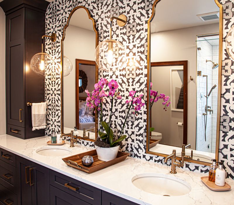 Black and white encaustic tiles, gold-rimmed arch mirrors, and dark cabinetry give old world charm to this sumptuous bathroom.