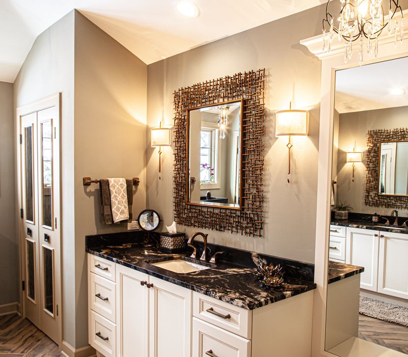 Bronze crosshatched mirror frames, herringbone wood look floor tile, and a vaulted ceiling add distinction to this two vanity bathroom.