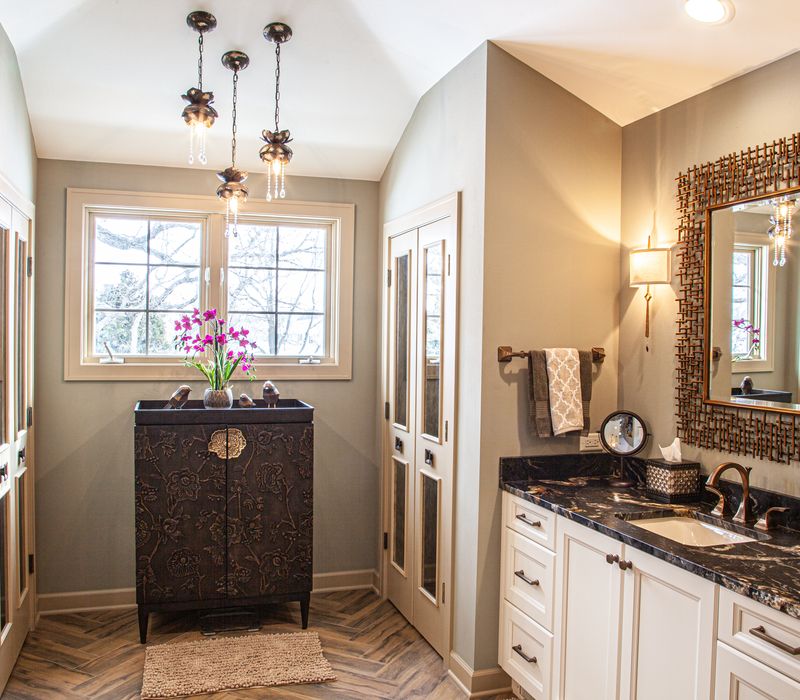 Bronze crosshatched mirror frames, herringbone wood look floor tile, and a vaulted ceiling add distinction to this two vanity bathroom.