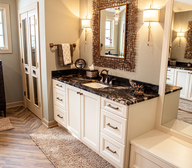 Bronze crosshatched mirror frames, herringbone wood look floor tile, and a vaulted ceiling add distinction to this two vanity bathroom.