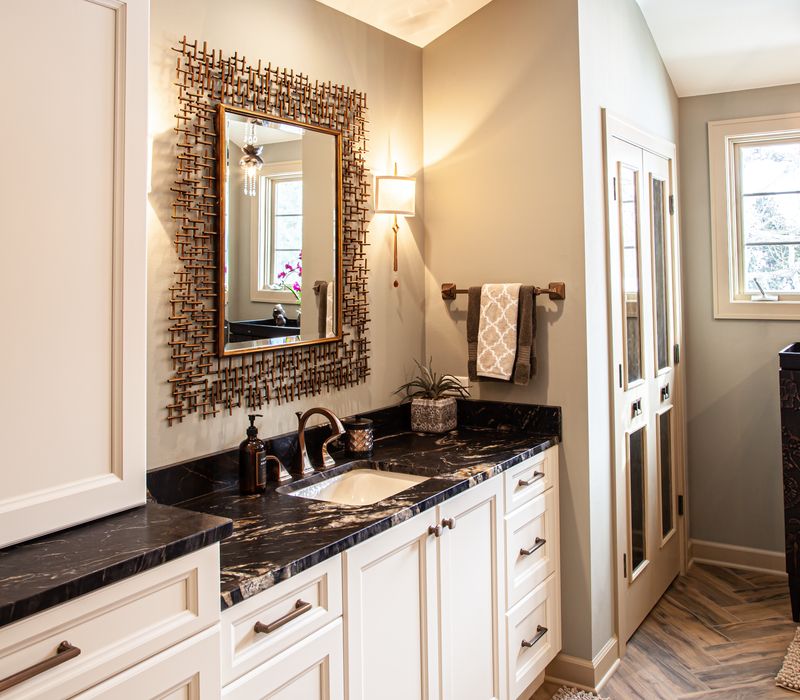 Bronze crosshatched mirror frames, herringbone wood look floor tile, and a vaulted ceiling add distinction to this two vanity bathroom.