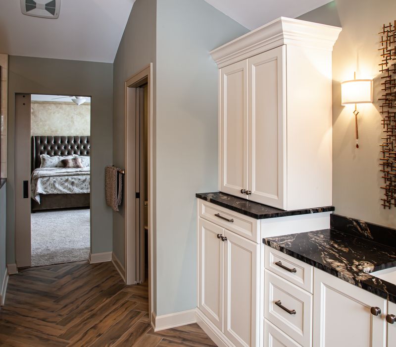 Bronze crosshatched mirror frames, herringbone wood look floor tile, and a vaulted ceiling add distinction to this two vanity bathroom.