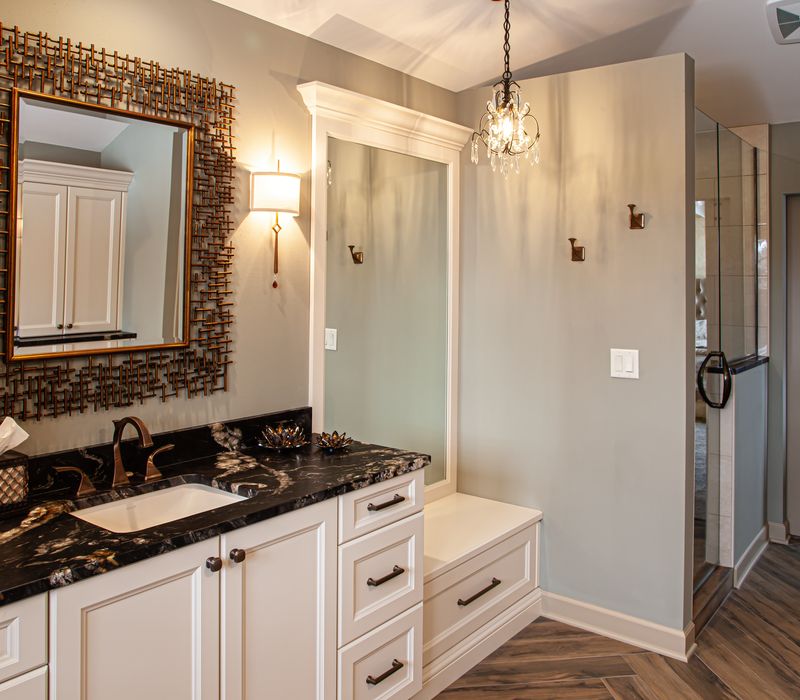Bronze crosshatched mirror frames, herringbone wood look floor tile, and a vaulted ceiling add distinction to this two vanity bathroom.