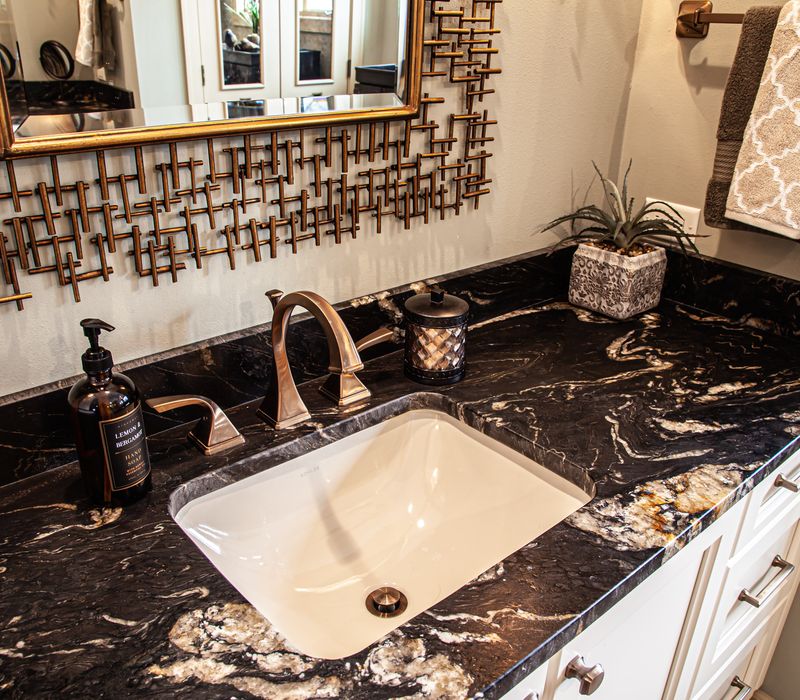 Bronze crosshatched mirror frames, herringbone wood look floor tile, and a vaulted ceiling add distinction to this two vanity bathroom.
