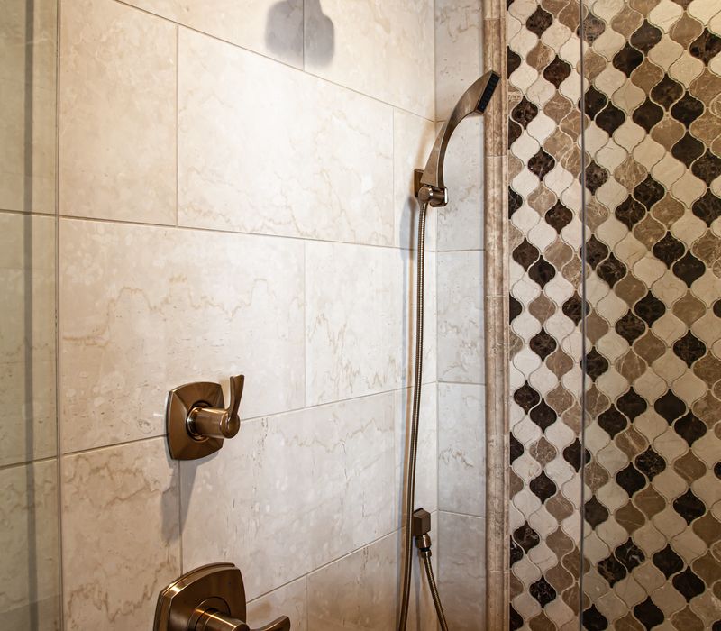Bronze crosshatched mirror frames, herringbone wood look floor tile, and a vaulted ceiling add distinction to this two vanity bathroom.