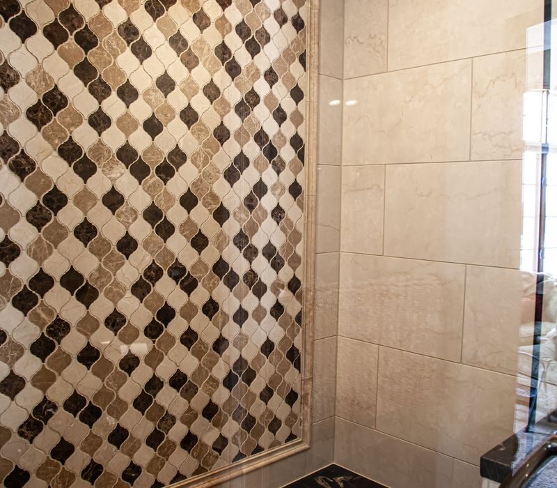 Bronze crosshatched mirror frames, herringbone wood look floor tile, and a vaulted ceiling add distinction to this two vanity bathroom.