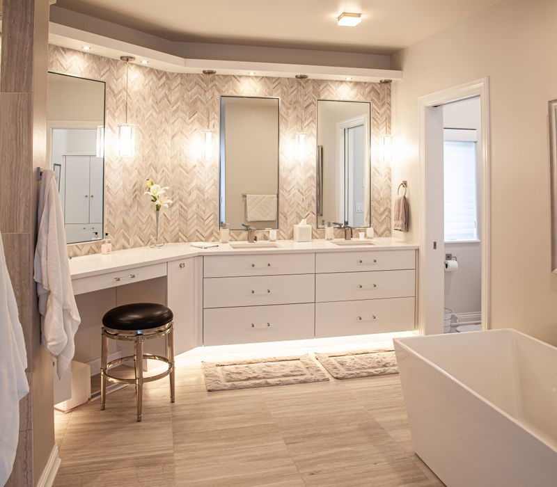 The neutral colors of the chevron wall tiles, spacious tiled walk-in shower, minimalist cabinetry, and a modern freestanding tub all set off the painting that is the centerpiece of this bathroom.