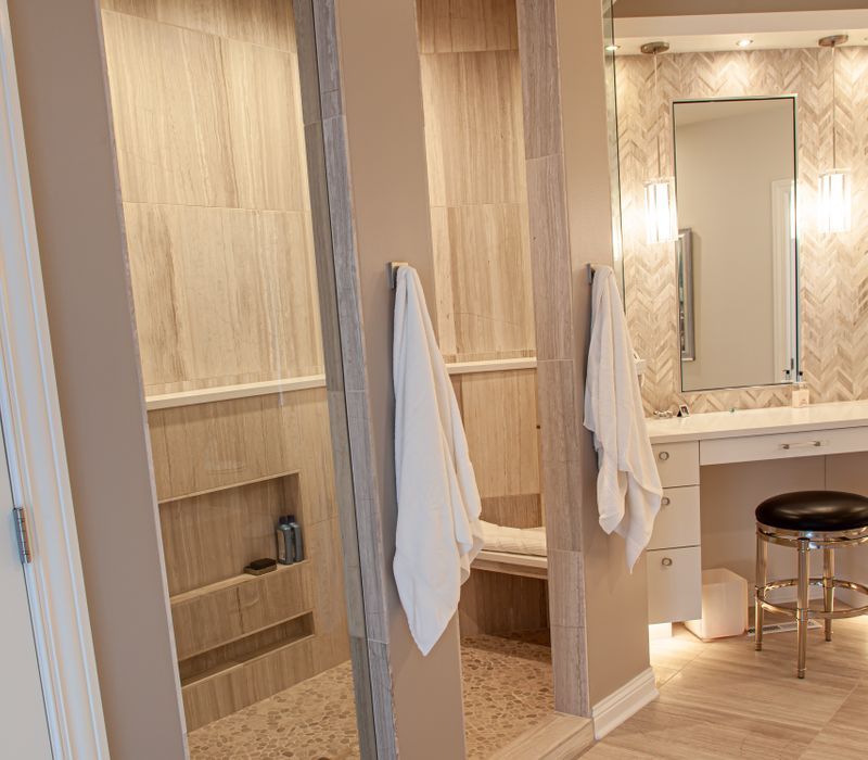 The neutral colors of the chevron wall tiles, spacious tiled walk-in shower, minimalist cabinetry, and a modern freestanding tub all set off the painting that is the centerpiece of this bathroom.