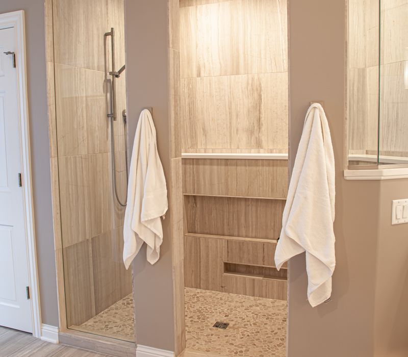 The neutral colors of the chevron wall tiles, spacious tiled walk-in shower, minimalist cabinetry, and a modern freestanding tub all set off the painting that is the centerpiece of this bathroom.