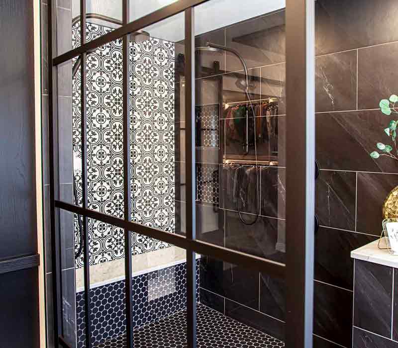 Elegance reigns supreme in this bathroom remodel that features an en suite, walk-in closet, walk-in shower, custom double vanity, private water closet, framed-glass barn doors, and a dazzling starburst chandelier.