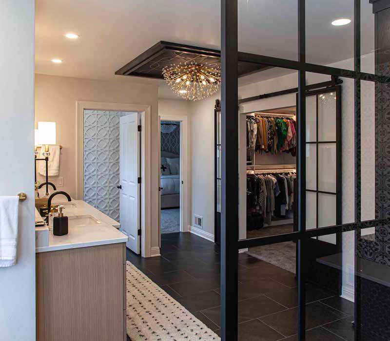 Elegance reigns supreme in this bathroom remodel that features an en suite, walk-in closet, walk-in shower, custom double vanity, private water closet, framed-glass barn doors, and a dazzling starburst chandelier.