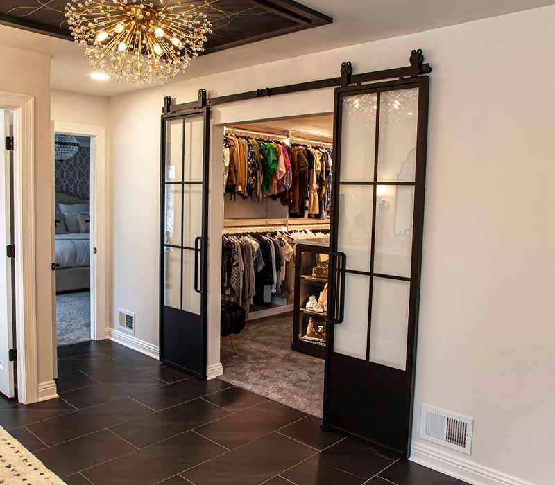 Elegance reigns supreme in this bathroom remodel that features an en suite, walk-in closet, walk-in shower, custom double vanity, private water closet, framed-glass barn doors, and a dazzling starburst chandelier.