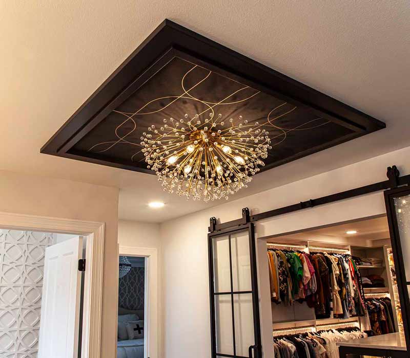 Elegance reigns supreme in this bathroom remodel that features an en suite, walk-in closet, walk-in shower, custom double vanity, private water closet, framed-glass barn doors, and a dazzling starburst chandelier.