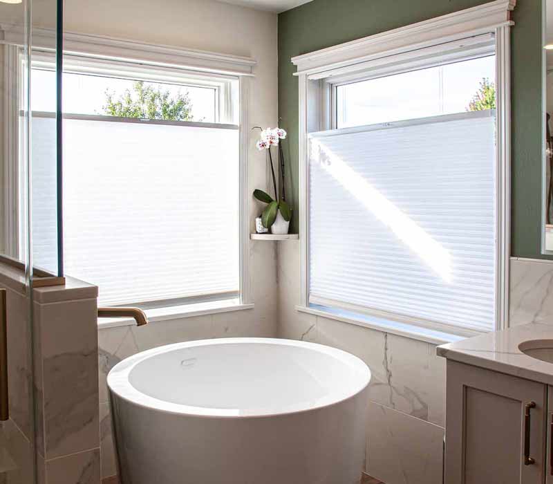 The pairing of cool stone and earthy tones in this bathroom remodel evokes the hush of a private spa. The bathroom features a Japanese soaking tub, custom double vanity, shower with dual showerheads, and lots of natural light.