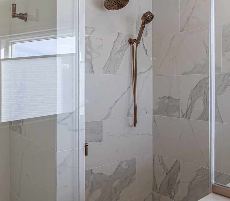 The pairing of cool stone and earthy tones in this bathroom remodel evokes the hush of a private spa. The bathroom features a Japanese soaking tub, custom double vanity, shower with dual showerheads, and lots of natural light.