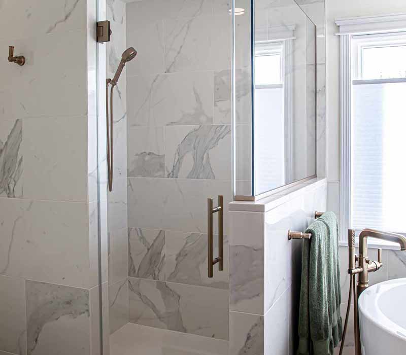 The pairing of cool stone and earthy tones in this bathroom remodel evokes the hush of a private spa. The bathroom features a Japanese soaking tub, custom double vanity, shower with dual showerheads, and lots of natural light.