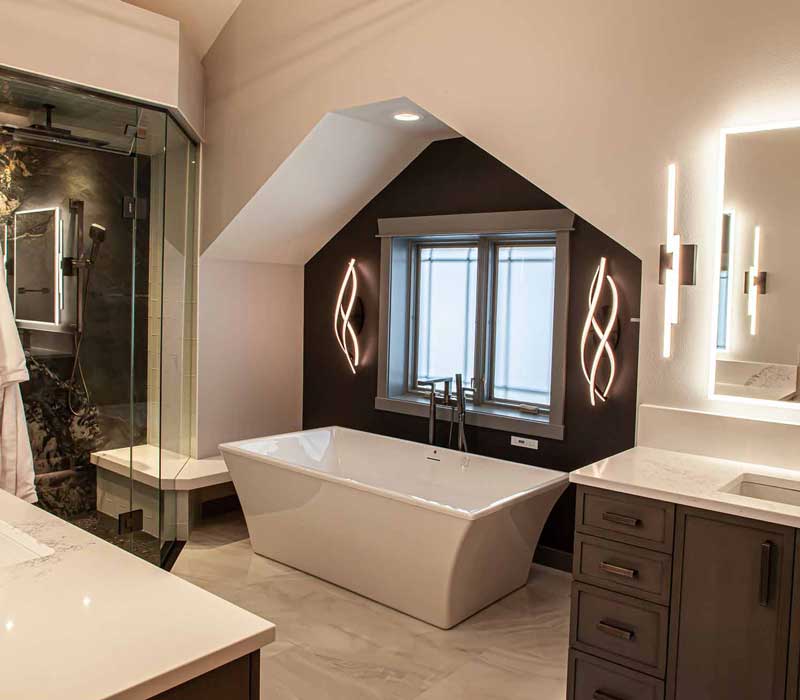This bathroom features a freestanding tub in an alcove, set off by a dark accent wall with two modern sconces and a glass shower stall with a marble wall.