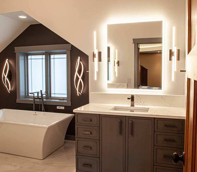 This bathroom features a freestanding tub in an alcove, set off by a dark accent wall with two modern sconces and a glass shower stall with a marble wall.