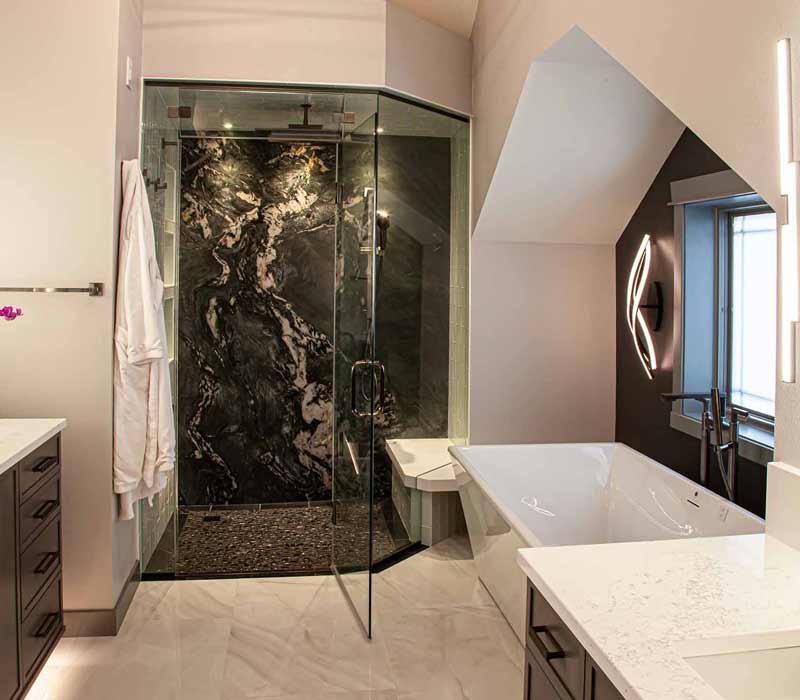 This bathroom features a freestanding tub in an alcove, set off by a dark accent wall with two modern sconces and a glass shower stall with a marble wall.