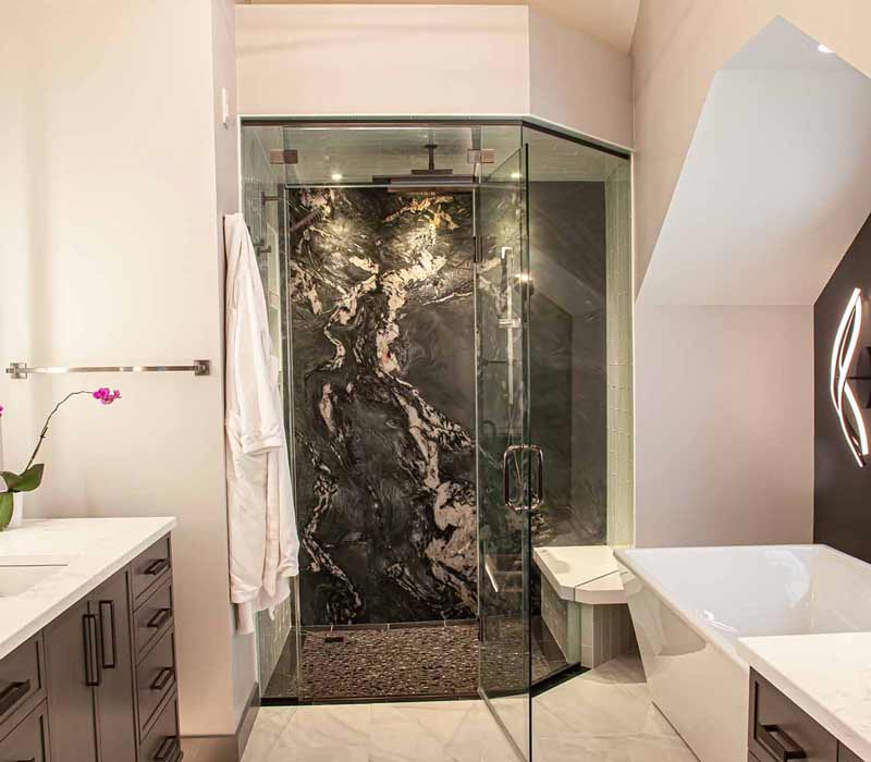 This bathroom features a freestanding tub in an alcove, set off by a dark accent wall with two modern sconces and a glass shower stall with a marble wall.