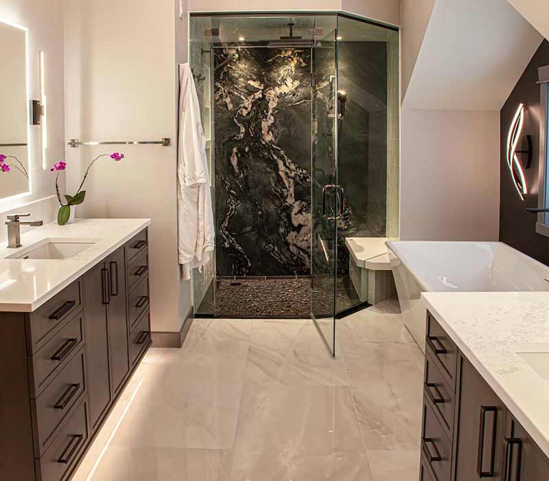 This bathroom features a freestanding tub in an alcove, set off by a dark accent wall with two modern sconces and a glass shower stall with a marble wall.