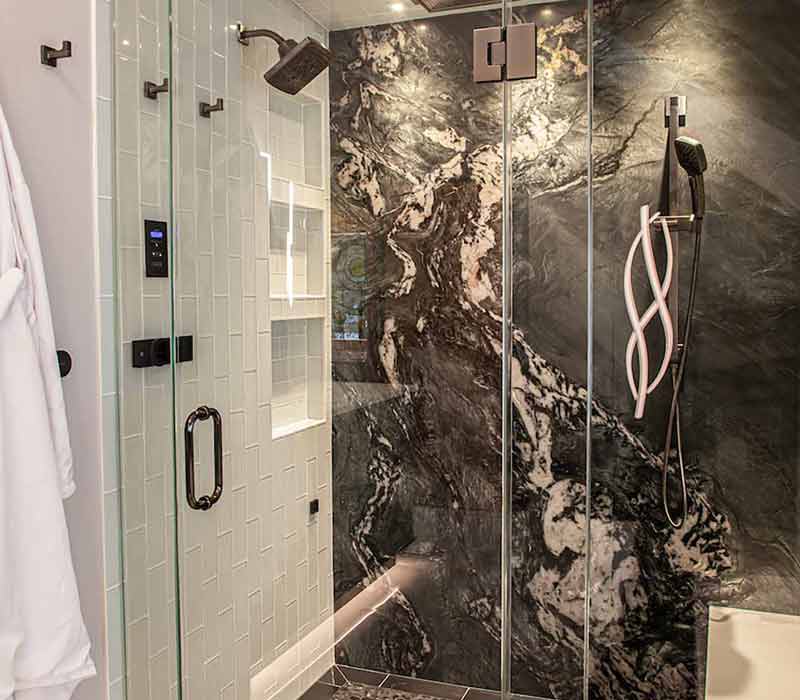 This bathroom features a freestanding tub in an alcove, set off by a dark accent wall with two modern sconces and a glass shower stall with a marble wall.