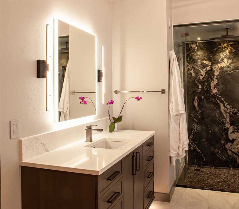 This bathroom features a freestanding tub in an alcove, set off by a dark accent wall with two modern sconces and a glass shower stall with a marble wall.