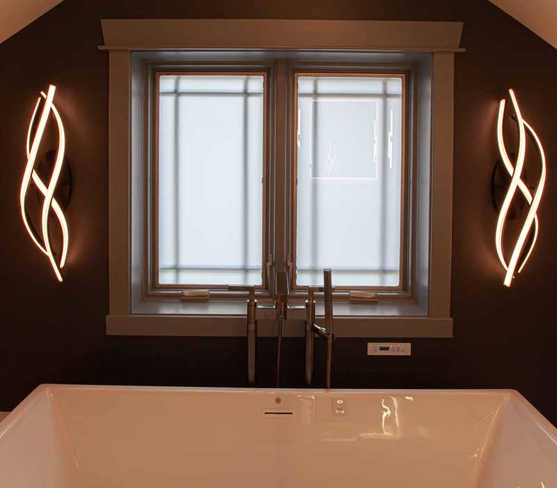This bathroom features a freestanding tub in an alcove, set off by a dark accent wall with two modern sconces and a glass shower stall with a marble wall.