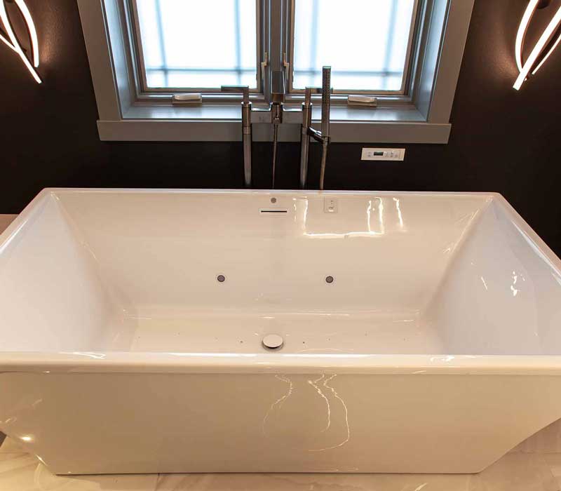 This bathroom features a freestanding tub in an alcove, set off by a dark accent wall with two modern sconces and a glass shower stall with a marble wall.