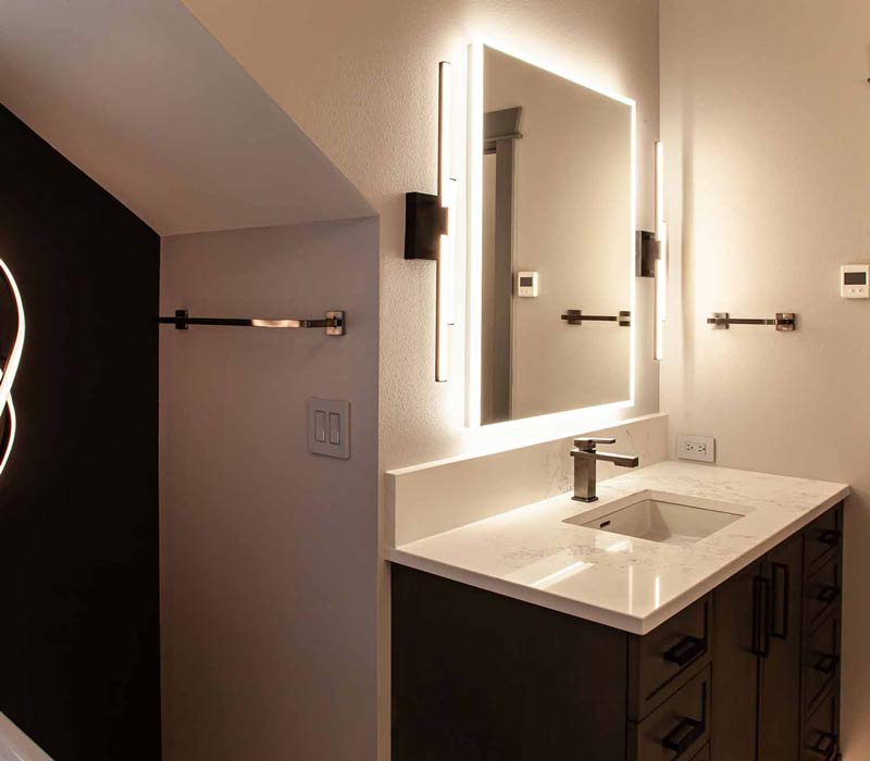 This bathroom features a freestanding tub in an alcove, set off by a dark accent wall with two modern sconces and a glass shower stall with a marble wall.