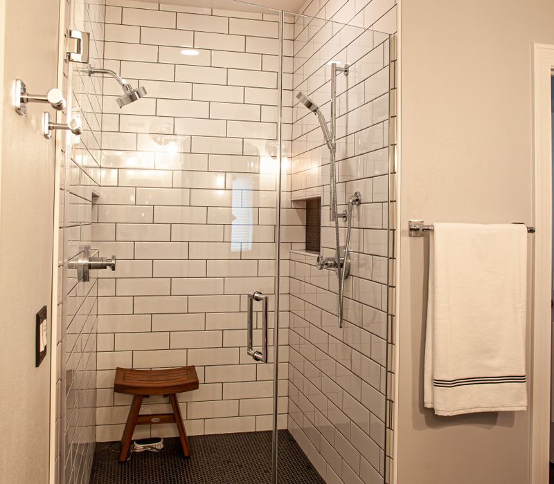 A retro inspired bathroom with a black and white freestanding tub, green glass accents, white subway tiles with dark grout, chrome fixtures, and walnut cabinetry.