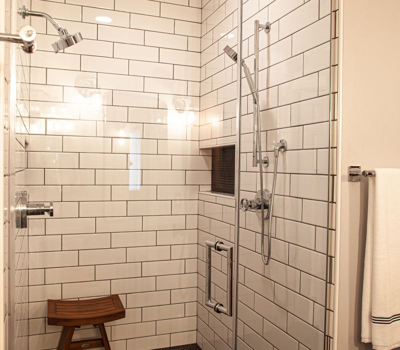 A retro inspired bathroom with a black and white freestanding tub, green glass accents, white subway tiles with dark grout, chrome fixtures, and walnut cabinetry.