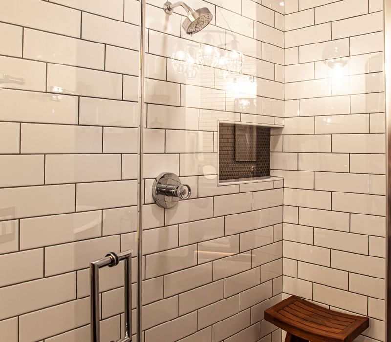 A retro inspired bathroom with a black and white freestanding tub, green glass accents, white subway tiles with dark grout, chrome fixtures, and walnut cabinetry.