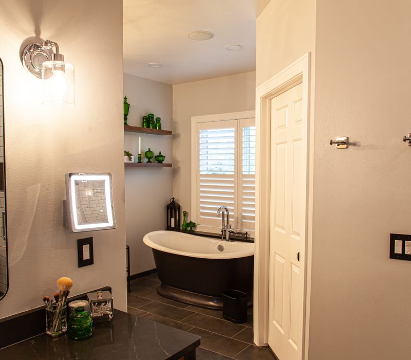 A retro inspired bathroom with a black and white freestanding tub, green glass accents, white subway tiles with dark grout, chrome fixtures, and walnut cabinetry.