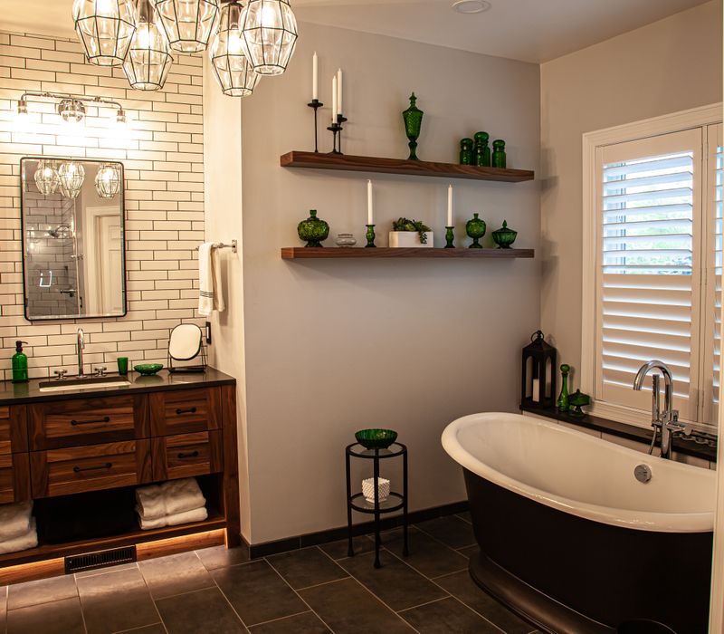 A retro inspired bathroom with a black and white freestanding tub, green glass accents, white subway tiles with dark grout, chrome fixtures, and walnut cabinetry.