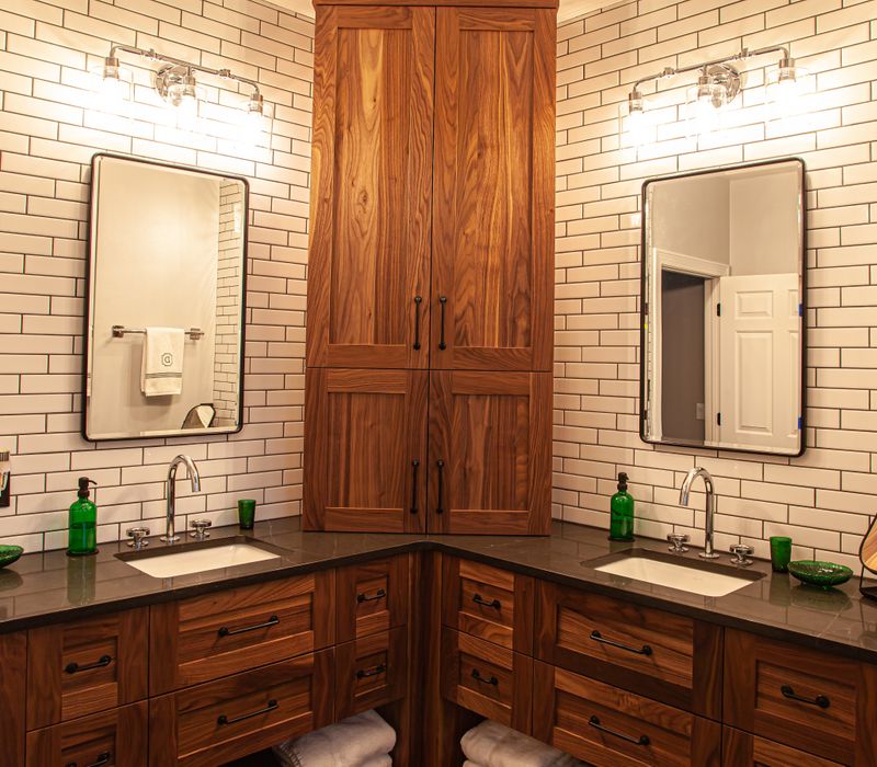 A retro inspired bathroom with a black and white freestanding tub, green glass accents, white subway tiles with dark grout, chrome fixtures, and walnut cabinetry.