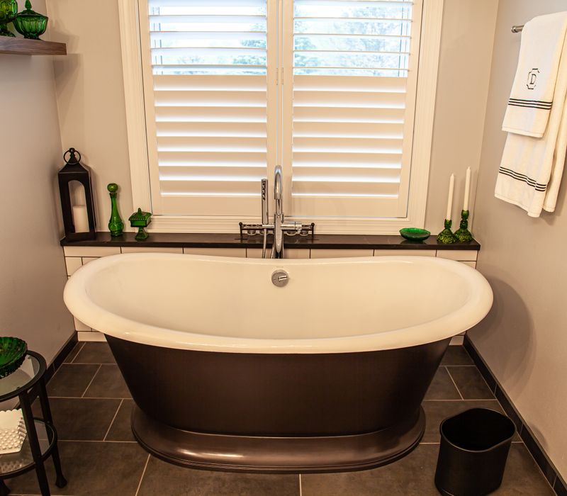 A retro inspired bathroom with a black and white freestanding tub, green glass accents, white subway tiles with dark grout, chrome fixtures, and walnut cabinetry.