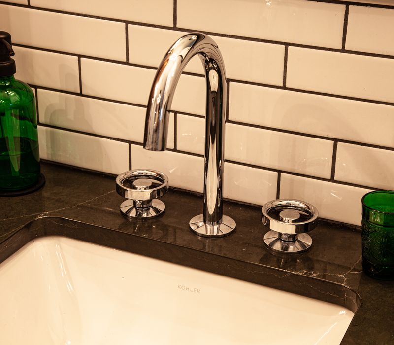 A retro inspired bathroom with a black and white freestanding tub, green glass accents, white subway tiles with dark grout, chrome fixtures, and walnut cabinetry.
