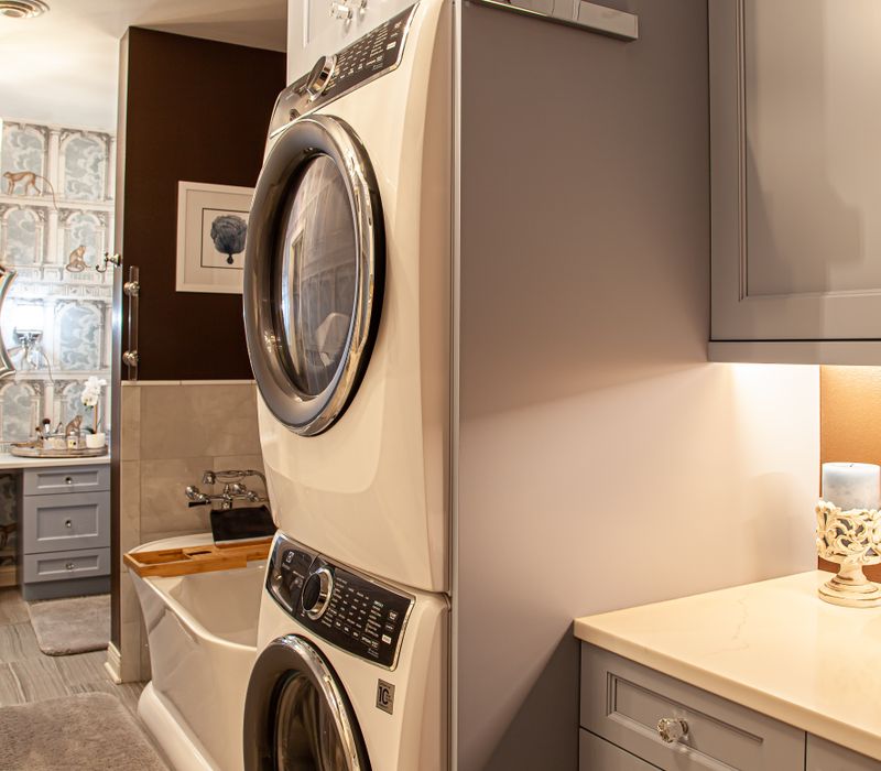 Wallpaper featuring monkeys posing on Venetian architecture, light blue cabinets, and elongated hexagon mosaic tiles add interest to this elegant bathroom with laundry machines and an attached walk-in closet.
