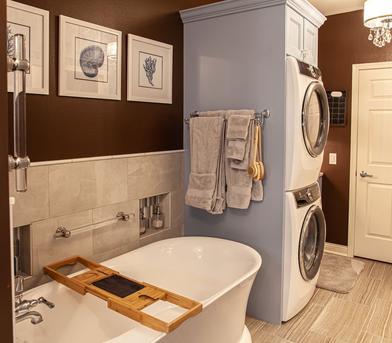 Wallpaper featuring monkeys posing on Venetian architecture, light blue cabinets, and elongated hexagon mosaic tiles add interest to this elegant bathroom with laundry machines and an attached walk-in closet.