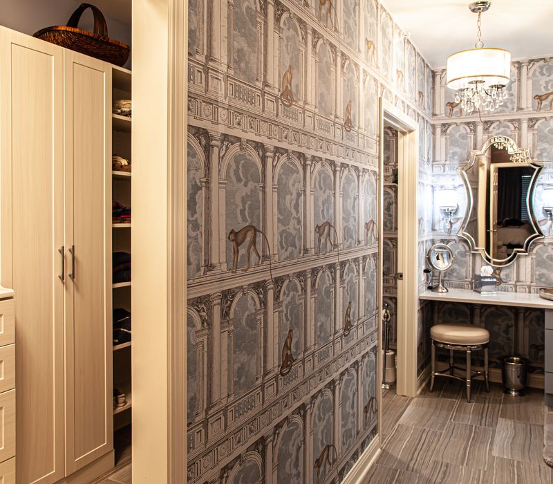 Wallpaper featuring monkeys posing on Venetian architecture, light blue cabinets, and elongated hexagon mosaic tiles add interest to this elegant bathroom with laundry machines and an attached walk-in closet.