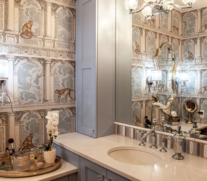 Wallpaper featuring monkeys posing on Venetian architecture, light blue cabinets, and elongated hexagon mosaic tiles add interest to this elegant bathroom with laundry machines and an attached walk-in closet.