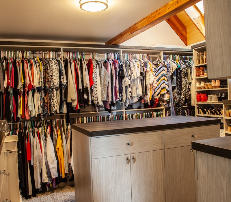 This walk-in closet features wooden ceiling beams that coordinate with the rest of the house, as well as a skylight, central counter, and lots of storage space in the modern cabinets.