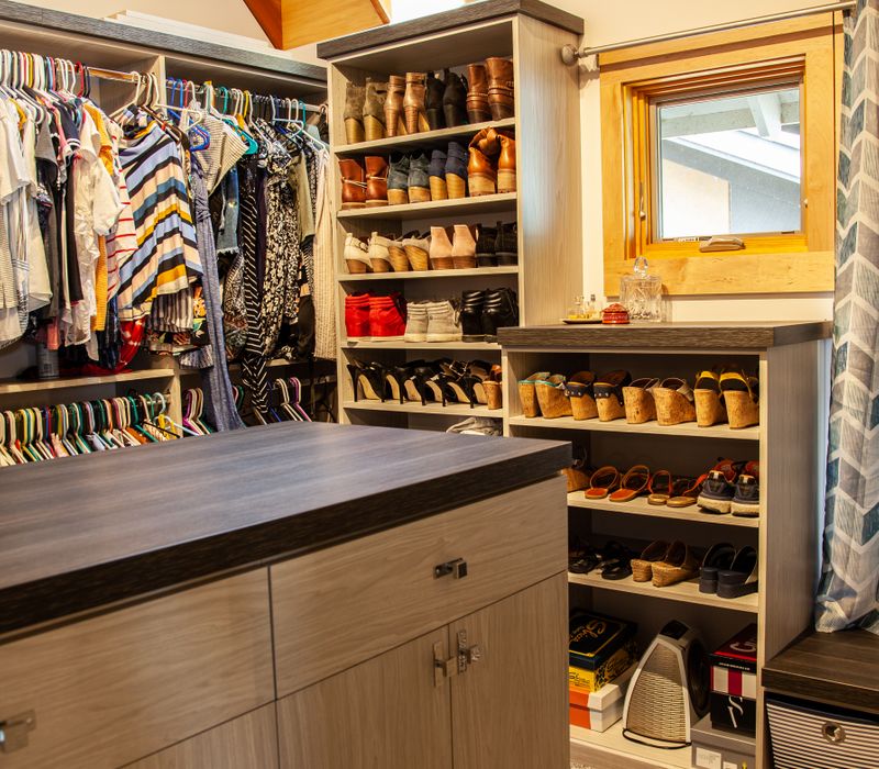 This walk-in closet features wooden ceiling beams that coordinate with the rest of the house, as well as a skylight, central counter, and lots of storage space in the modern cabinets.