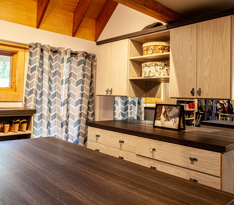 This walk-in closet features wooden ceiling beams that coordinate with the rest of the house, as well as a skylight, central counter, and lots of storage space in the modern cabinets.