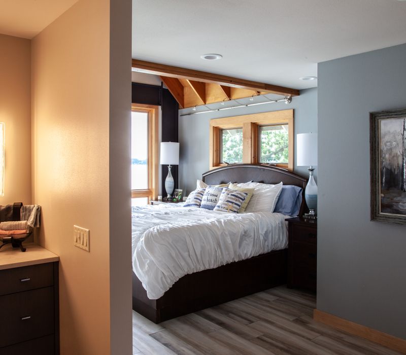 This walk-in closet features wooden ceiling beams that coordinate with the rest of the house, as well as a skylight, central counter, and lots of storage space in the modern cabinets.